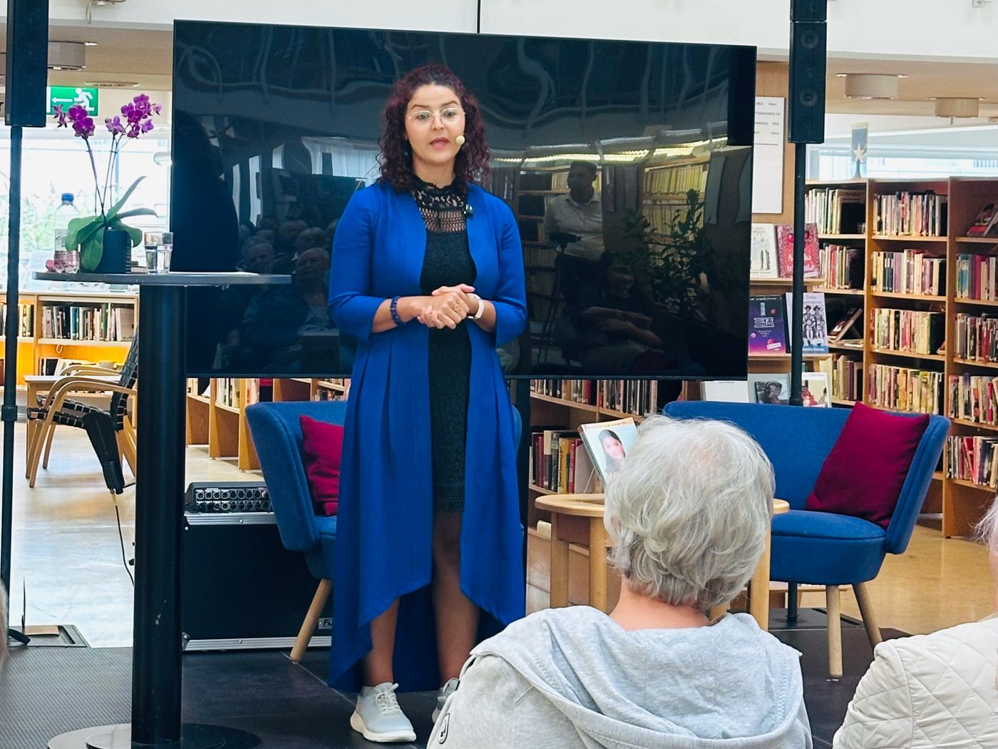 Maryam Jan Akbari talar på scen på Eskilstuna stadsbibliotek inför en full publik.